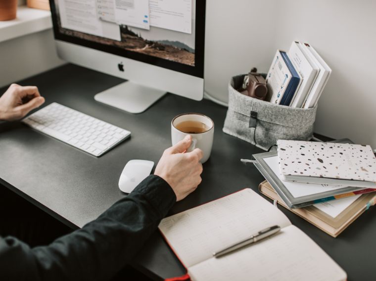 ersona trabajando frente a un ordenador con una taza de café y libretas